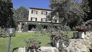 Un bâtiment en pierre doté d’un toit en pente, entouré d’une végétation luxuriante et de plantes en fleurs.