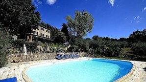 Une piscine avec des chaises bleues, un mur de pierre et un bâtiment en arrière-plan.