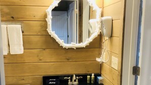A bathroom with a wooden wall, a white toilet, a black sink with a mirror above it, and a hairdryer on the wall. -  Knotty Squirrel Unit 2 King Suite with Ladder Loft (Mountain View)