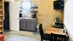 A compact kitchen with wooden walls, a built-in sink, and a dining area with a table and chairs. -  Knotty Squirrel Unit 2 King Suite with Ladder Loft (Mountain View)