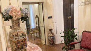 Une pièce avec un plancher en bois, un fauteuil recouvert d’un tissu rouge, un grand vase décoratif et un miroir.