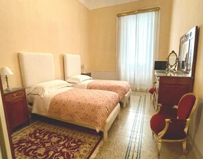 Ein Hotelzimmer mit zwei Betten, einem Schreibtisch, einem Stuhl, einem Spiegel und einem Fenster mit Vorhängen.
