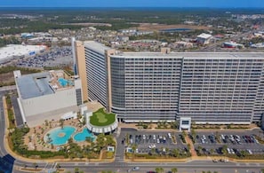 A large hotel with multiple floors, a swimming pool, and a parking lot.