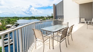 Un balcone con tavolo e sedie in vetro, vista su uno specchio d'acqua e sullo skyline della città.