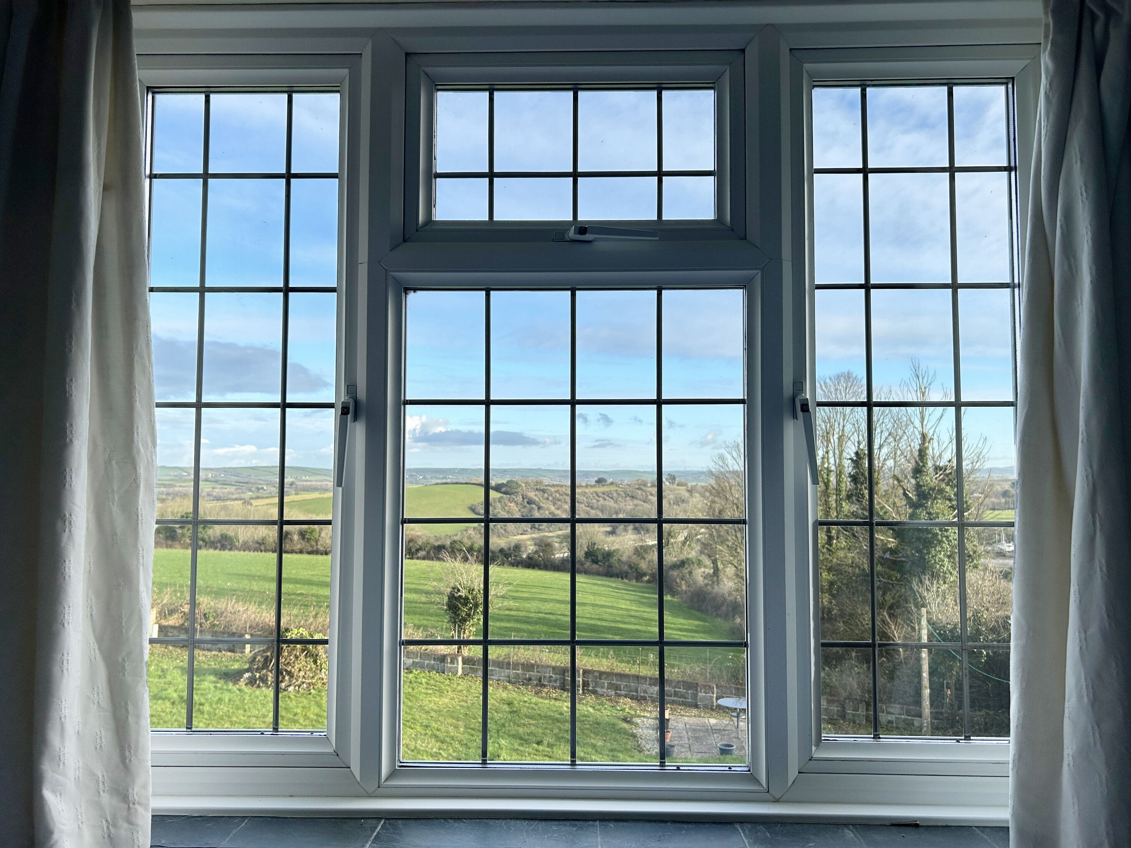 A room with three large windows offering a view of a green landscape.