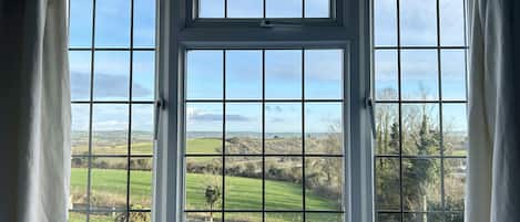 A room with three large windows offering a view of a green landscape.