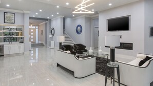A modern living room with a white sofa, black chairs, a glass coffee table, and a TV mounted on the wall. - White House at Reunion | 10BR Luxe Stay w/ Bowling Alley, Arcade, Private Pool, and Gym Near Disney (Kissimmee)