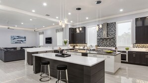 A modern kitchen with a large island, dark cabinetry, and pendant lighting. - White House at Reunion | 10BR Luxe Stay w/ Bowling Alley, Arcade, Private Pool, and Gym Near Disney (Kissimmee)