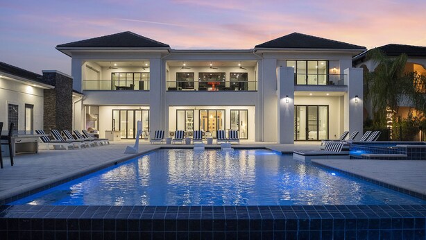 A modern two-story house with a swimming pool, outdoor seating, and a well-lit entrance. - White House at Reunion | 10BR Luxe Stay w/ Bowling Alley, Arcade, Private Pool, and Gym Near Disney (Kissimmee)
