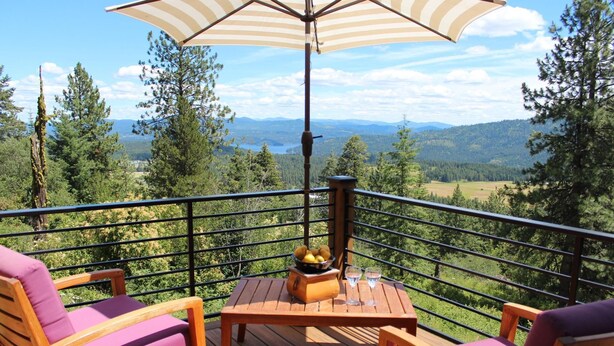 Eine Holzterrasse mit zwei Stühlen, einem Tisch, einem Sonnenschirm und einem Holzofen.