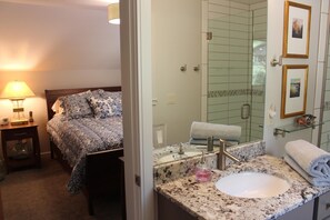 Hotellihuone, jossa on sänky, yöpöytä, lamppu sekä kylpyhuone, jossa on pesuallas, peili ja suihku.