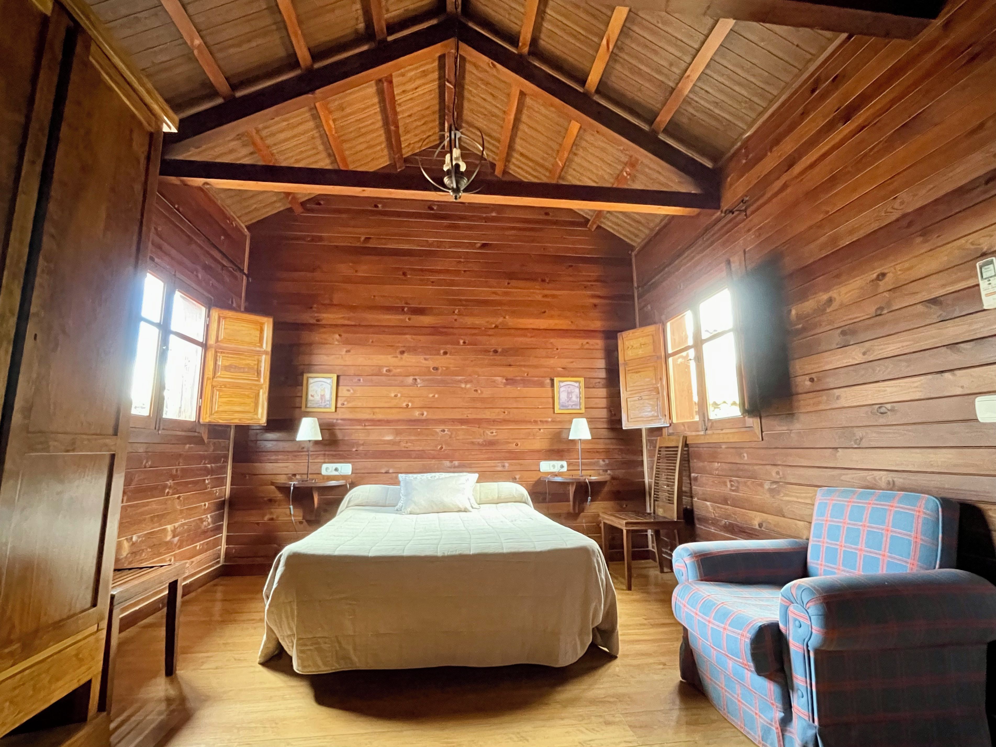 A wooden cabin room with a bed, two bedside tables, a chair, and a ceiling fan.