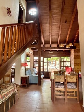 A spacious living area with a wooden staircase, a dining table with chairs, a sofa, and a window providing natural light. - Rural house capacity from 2 to 16 people, house for 12 and suitable for 2/4 pax (San Carlos del Valle)