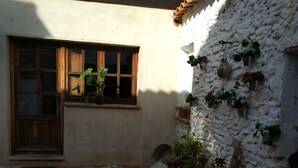 A courtyard with a tiled floor, a wooden door, a window with a plant, and a white wall with potted plants. - Rural house capacity from 2 to 16 people, house for 12 and suitable for 2/4 pax (San Carlos del Valle)