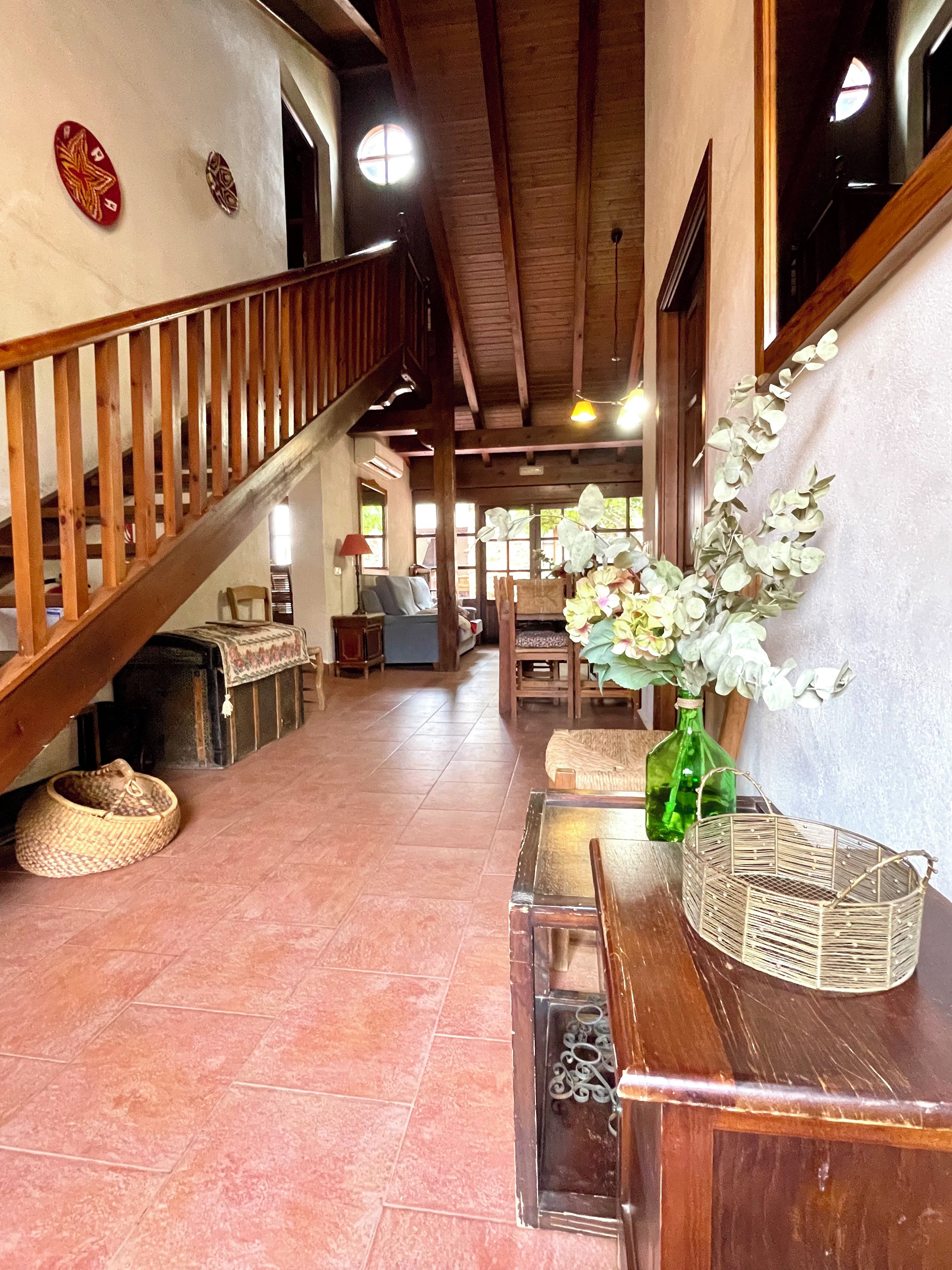 Un hall d’entrée spacieux avec un escalier en bois, un banc et un vase rempli de fleurs.