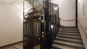 Een trap met een zwarte metalen leuning en een glazen lift.