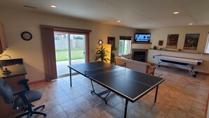 A living room with a ping pong table, a TV, a fireplace, and a large window.
