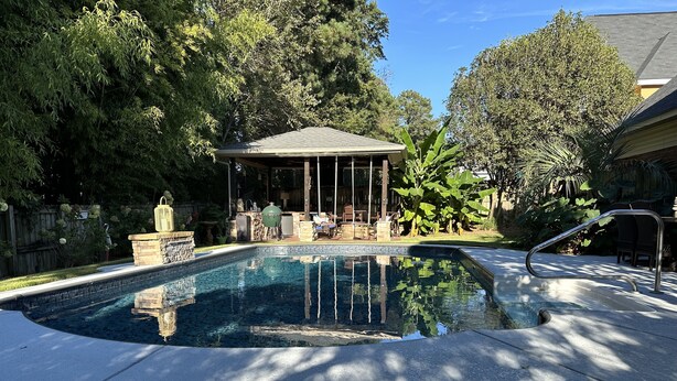 Piscina com um gazebo, escadas de pedra e vegetação ao redor.