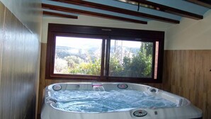 A hot tub with a view of a mountainous landscape through a large window.