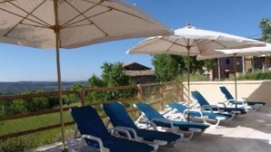 A poolside area with lounge chairs and umbrellas, overlooking a scenic landscape.