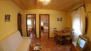 A cozy room with a wooden ceiling, a sofa, a dining table with chairs, and a television.