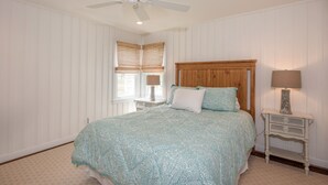 Una camera da letto con un letto, una ventola a soffitto, un comodino con una lampada e una finestra con persiane.