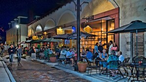 Ein Straßencafé mit Tischen und Stühlen, Personen beim Essen und Geschäfte in der Straße.