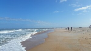 Ein weiter Sandstrand mit sanften Wellen und blauem, wolkenlosem Himmel.