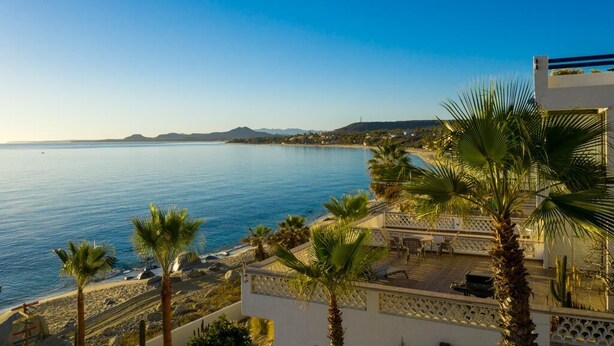 A coastal view with a clear sky, a beach, and a building with a balcony overlooking the sea. - Tranquil and Relaxing Beachfront Condo with Exceptional Views! (Los Barriles)