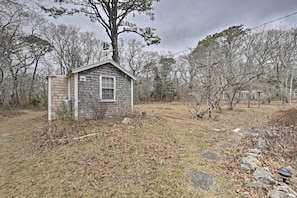 Situated in a natural setting, this small cabin features a gabled roof and is surrounded by trees and shrubs.