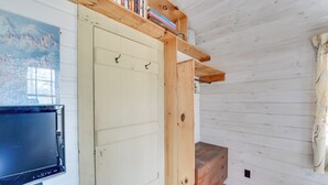 Um quarto com um suporte de TV de madeira, uma porta branca com ganchos e uma estante com livros.