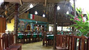 A restaurant with wooden chairs and tables, a thatched roof, and a mural on the wall. - Hotel Nueva Alianza (Ocosingo)