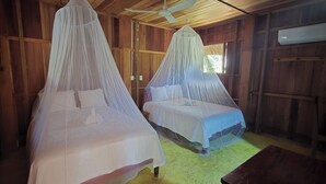 Two beds with mosquito netting, wooden walls, a ceiling fan, and an air conditioning unit. - Hotel Nueva Alianza (Ocosingo)