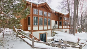 A wooden cabin with multiple windows, a covered outdoor seating area, and a staircase leading to the entrance. - Ski In/Ski Out on Boyneland, Slps 14 (Boyne Falls)