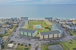 An aerial view of a coastal residential area with a central swimming pool surrounded by multi-story buildings. - Surf Condo 518 - HeavenLee By The Sea - First Floor End Unit (Surf City)
