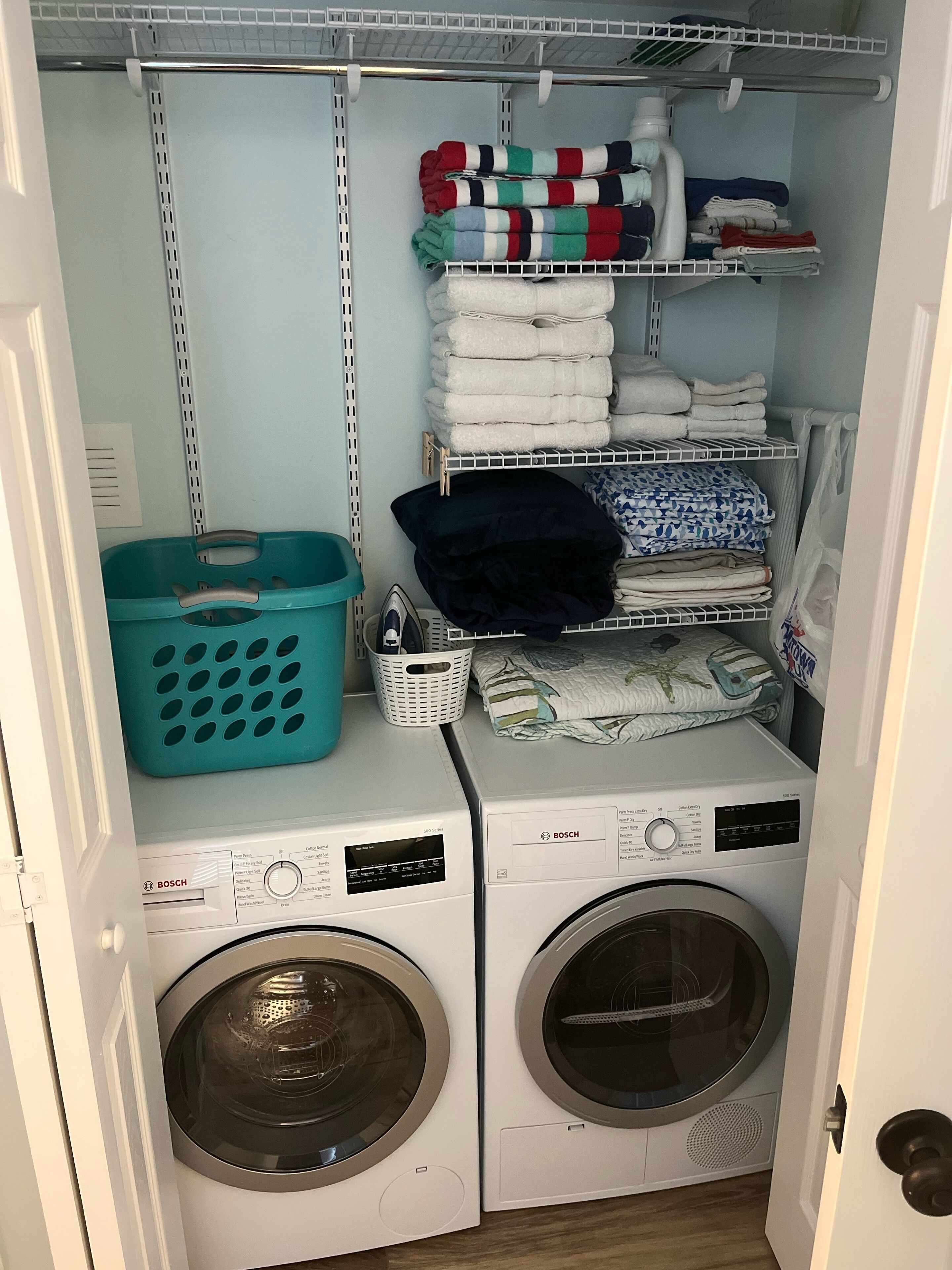 A laundry room with two Bosch washing machines, a shelf with folded towels, and a blue laundry basket.