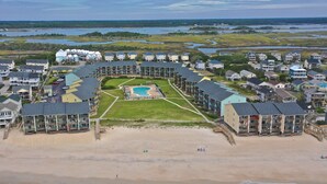 Un resort costero con piscina central, villas frente a la playa y vistas del agua circundante.
