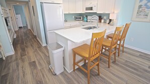 Una cocina con armarios blancos, microondas, lavamanos y sillas de madera.