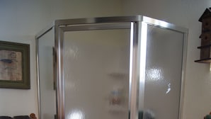 A corner shower enclosure with a glass door, a wicker basket, and a small rug on the floor. - Elk Haven Vacation Cabins, Custer SD, Elk Haven Vacation Cabins, Custer SD (Custer)