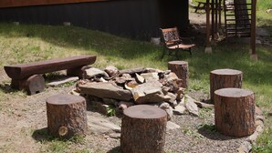 A rustic outdoor seating area with a wooden bench, a fire pit, and four wooden stools. - Elk Haven Vacation Cabins, Custer SD, Elk Haven Vacation Cabins, Custer SD (Custer)
