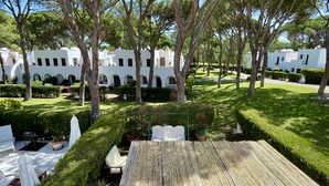 Une cour bordée de bâtiments blancs, d’arbres et d’une terrasse en bambou.