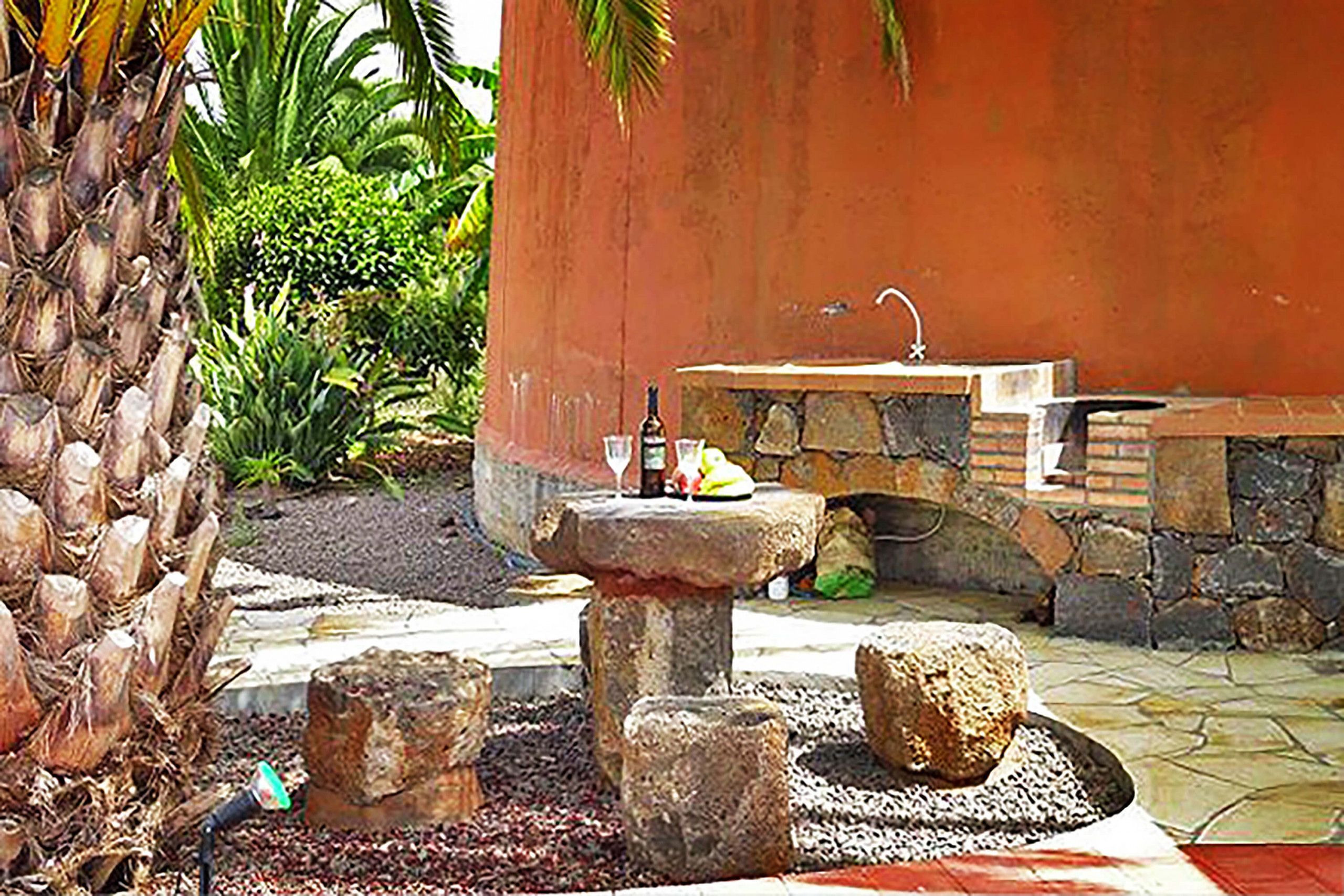 An outdoor patio with a stone sink, a small table with a bottle and glass, and a decorative rock arrangement.