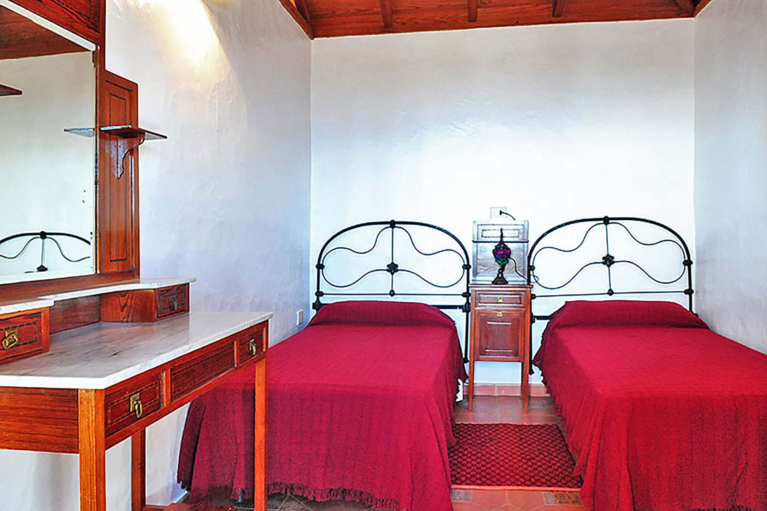 A room with two single beds, a wooden dresser, a mirror, and a small table with a lamp.