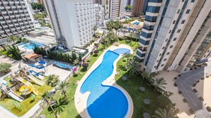 Una piscina rodeada de palmeras y una zona de juegos infantiles con toboganes.