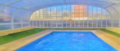 Una piscina interior con techo de cristal, agua transparente y un flotador.