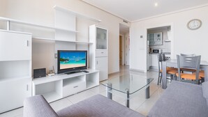 Una sala de estar moderna con un televisor de pantalla plana, una mesa de centro de vidrio y sofás grises.