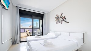 Habitación de hotel con dos camas, un balcón con mesa y sillas, y un adorno en la pared.