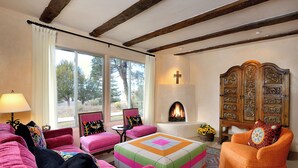 A cozy living room with a fireplace, a large window, and a wooden cabinet. - Casa Bohemia | Charming Retreat (Santa Fe)