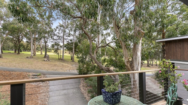 A balcony with a view of a grassy area and trees, a metal table, and a potted plant. - Ocean's Course (Lorne)