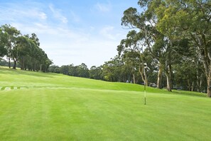 A golf course with a flagstick, trees, and a clear sky. - Ocean's Course (Lorne)